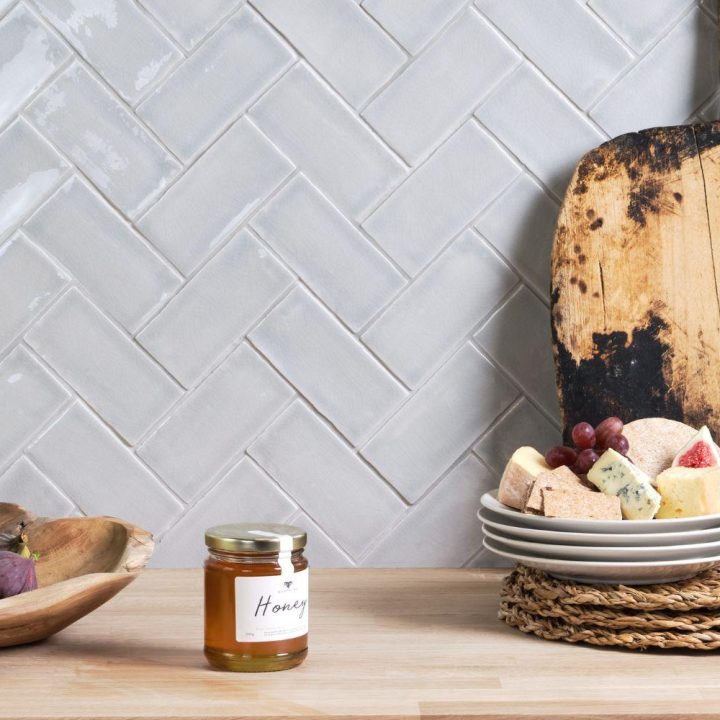 Small brick light grey Savernake College Fields wall tiles in a herringbone pattern on a kitchen wall behind a fruit bowl, wooden platter and glass of wine