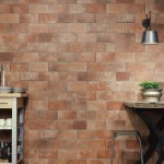 Wall of terracotta brick tiles in a brick bond pattern with grey grout behind a kitchen table an wall light