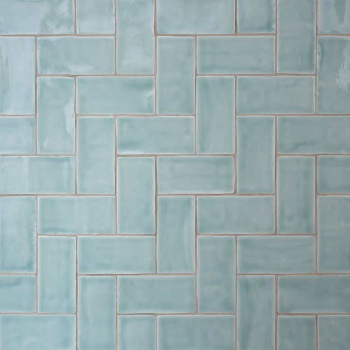 Wall of gloss cool blue medium metro tile laid in a vertical herringbone tile pattern finished with beige grout