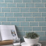Wall of a pale green blue medium brick metro tiles with beige grout against a stone worktop with a cookbook and herb planter