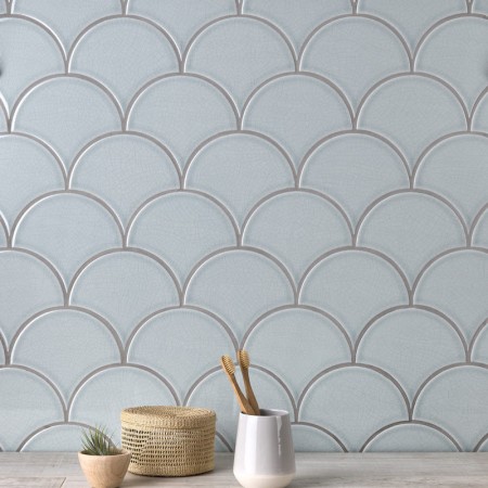Wall of pale silver blue scallop tiles with medium grey grout against an oak worktop behind some home accessories
