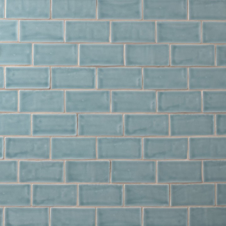 Wall of a pale blue green medium brick metro tiles with beige grout laid in a brick bond tile pattern