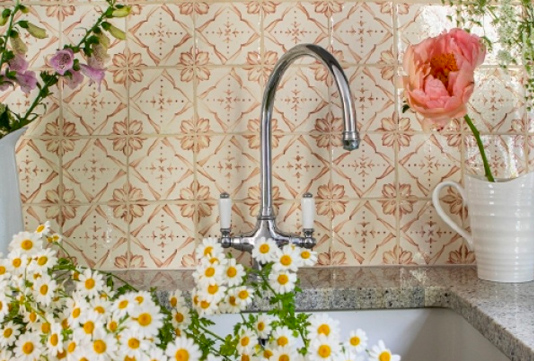 Floral tiles behind a chrome tap with white & yellow cut flowers in the foreground