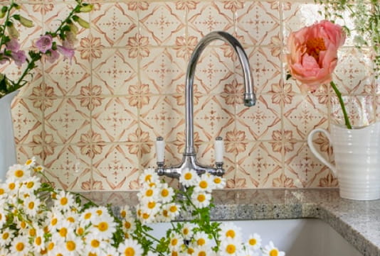 Floral tiles behind a chrome tap with white & yellow cut flowers in the foreground