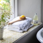 Windowsill filled with amber yellow Mediterranean tiles underneath a pile of towels and pot of daisies