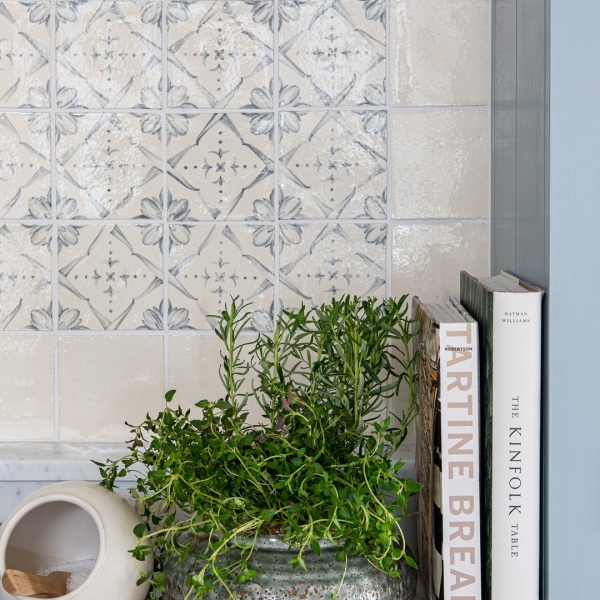 Wall of powder blue Mediterranean pattern hand painted tiles with a border of plain tiles behind kitchen accessories and a houseplant