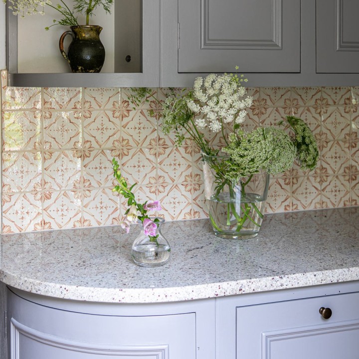 Wall of Mediterranean burnt orange handpainted wall tiles against a marble work top and pastel cabinetry