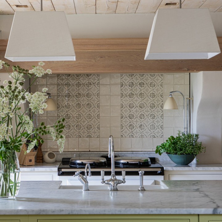 Wall of charcoal Mediterranean pattern hand painted tiles with a border of plain tiles behind a white aga and neutral cabinets