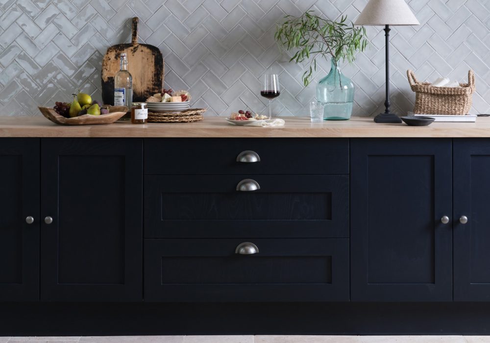 Navy kitchen cabinets with a french limestone porcelain floor and a wall of grey herringbone metro tiles