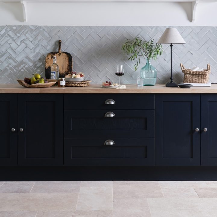 Navy kitchen cabinets with a french limestone porcelain floor and a wall of grey herringbone metro tiles