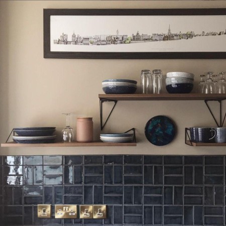 Dark blue metro brick wall tiles in Savernake Manton Hollow colour in a basketweave pattern below a wooden shelf and stone coloured painted wall in a kitchen