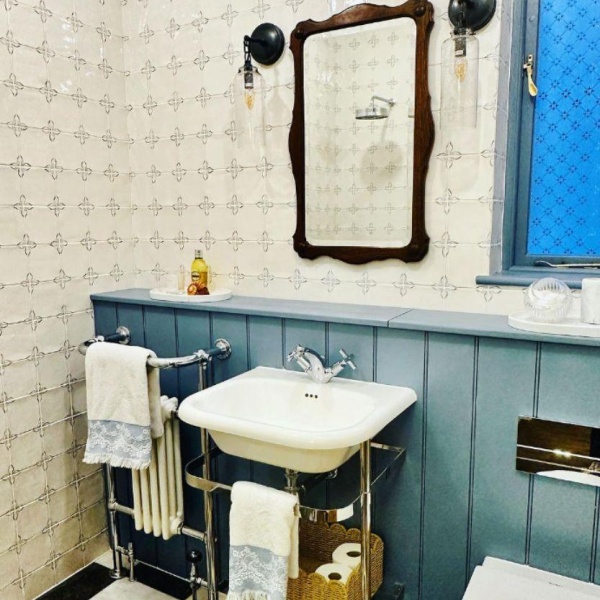 Delft handpainted floral corner motif wall tiles on the walls of a bathroom, above blue wooden panelling and white sink