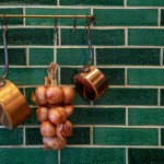 Isles Iona 6cm x 21cm skinny metro brick tiles in brick bond layout on a wall with hanging onions and copper pots in front