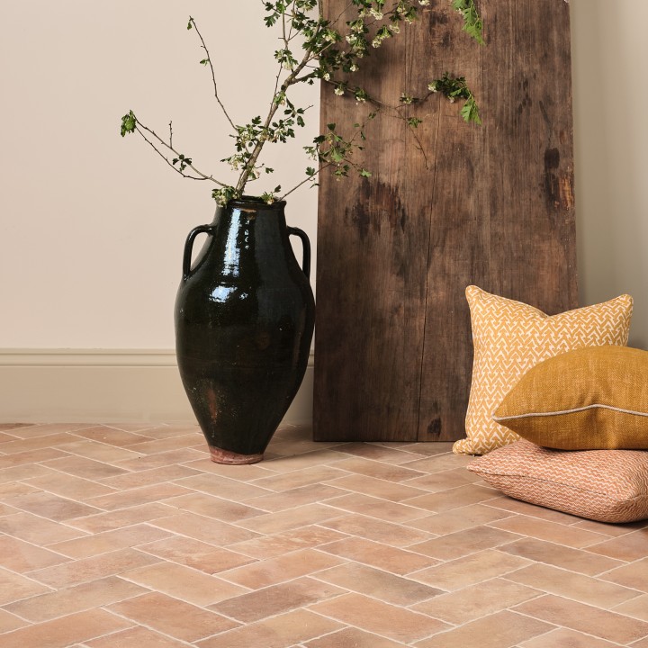 Pale terracotta Seville Small Brick tiles laid in a herringbone pattern on the floor with limestone grout with a vase and wood board in the background