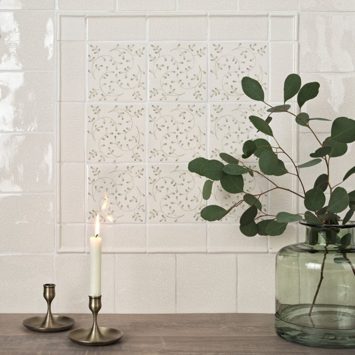 Wall of Emma Sage Green leaf Pattern Square tiles framed with half rounds and surrounded with Emma Sage Green Plain Square tiles behind dark wood oak top and green vase