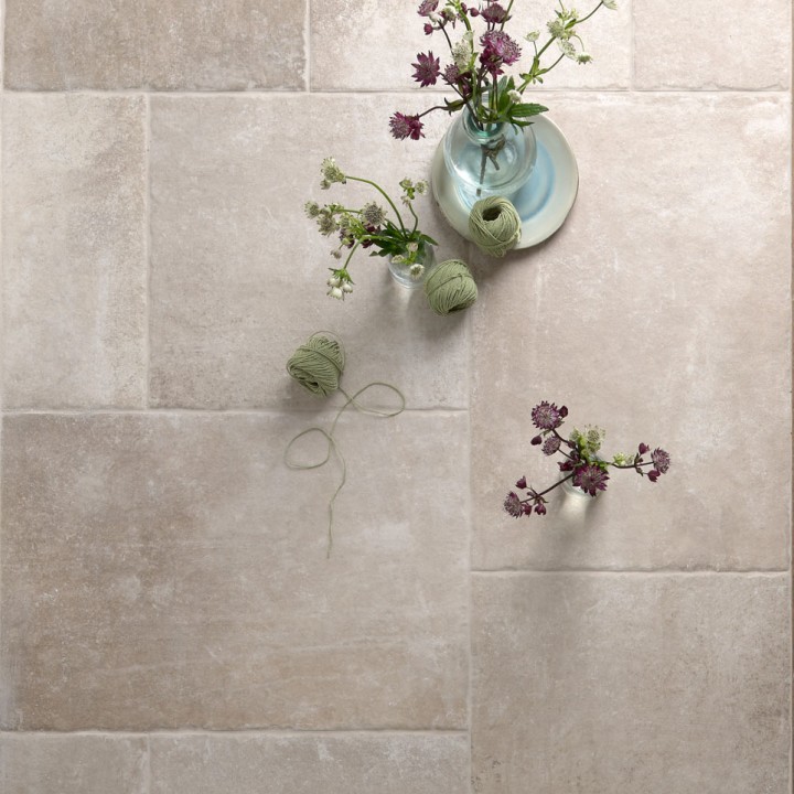 Floor of square and rectangle amber toned stone effect porcelain floor tiles with a vase and flowers on top