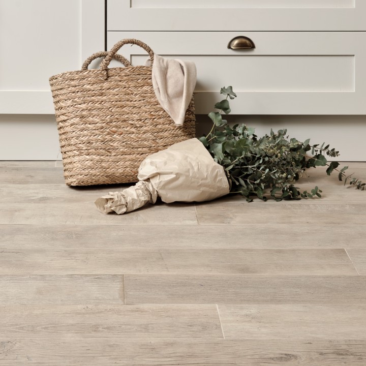 Pale wood effect floor laid in a straight pattern against white kitchen cabinets with a basket and bouquet of flowers on top