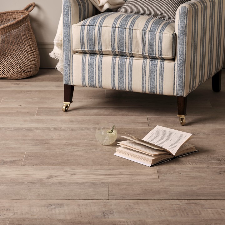 Wood effect floor laid in a straight pattern against cream wall with a chair and book in front