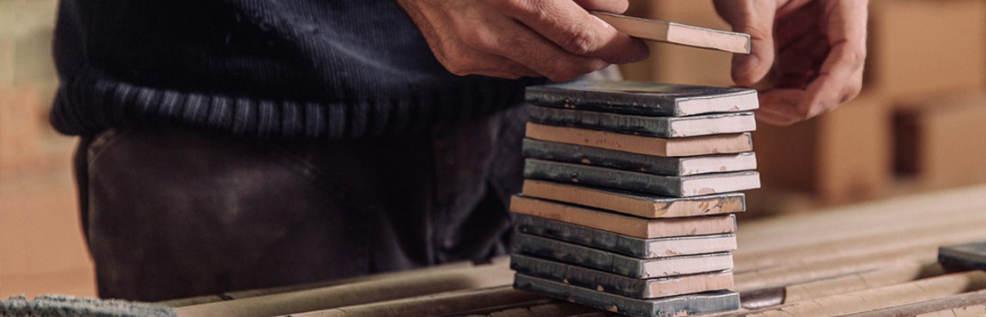 A close up of a stack of crackle glaze tiles with our makers stacking them on a line