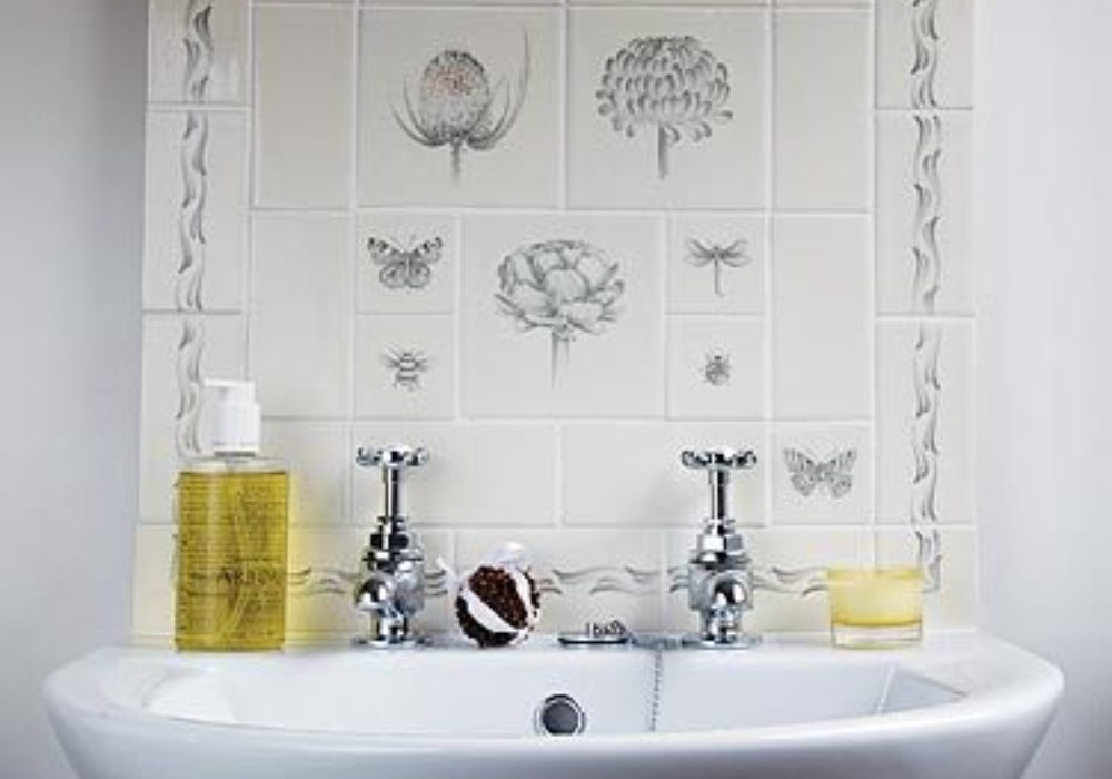 A wall of botanical tiles with flowers, butterflies and insects behind a sink with traditional taps