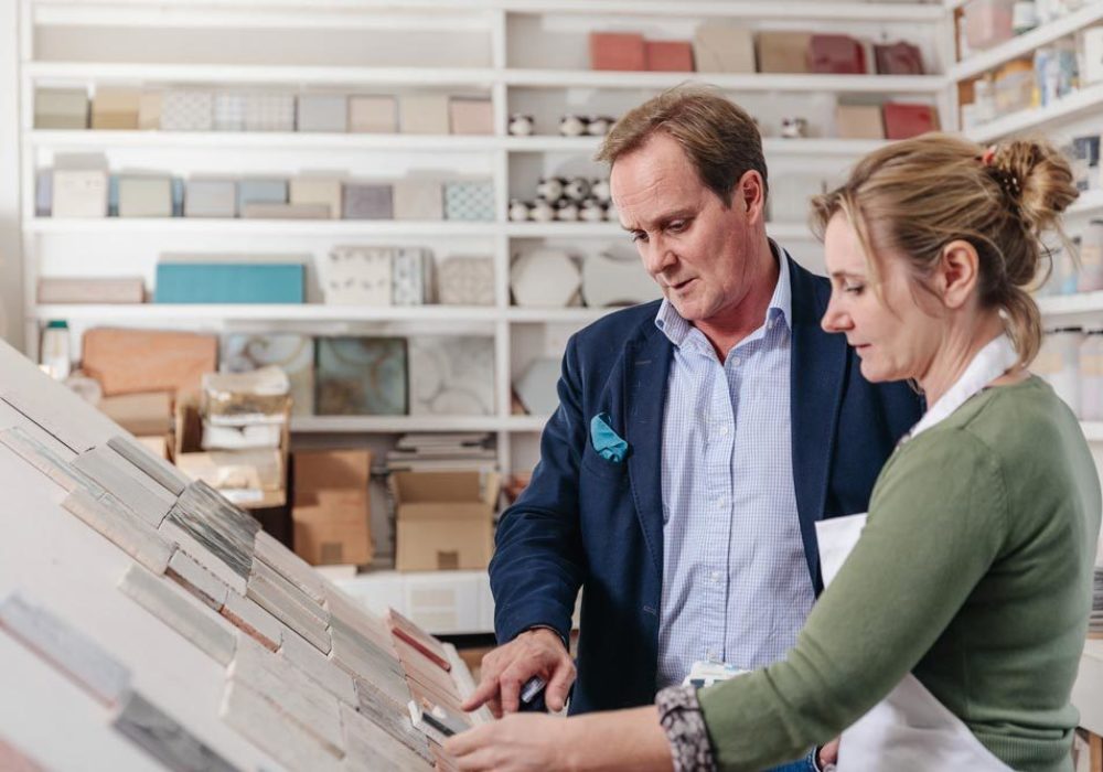 Close up of Jamie and Anita reviewing a tile collection in the lab with shelving of tiles behind.