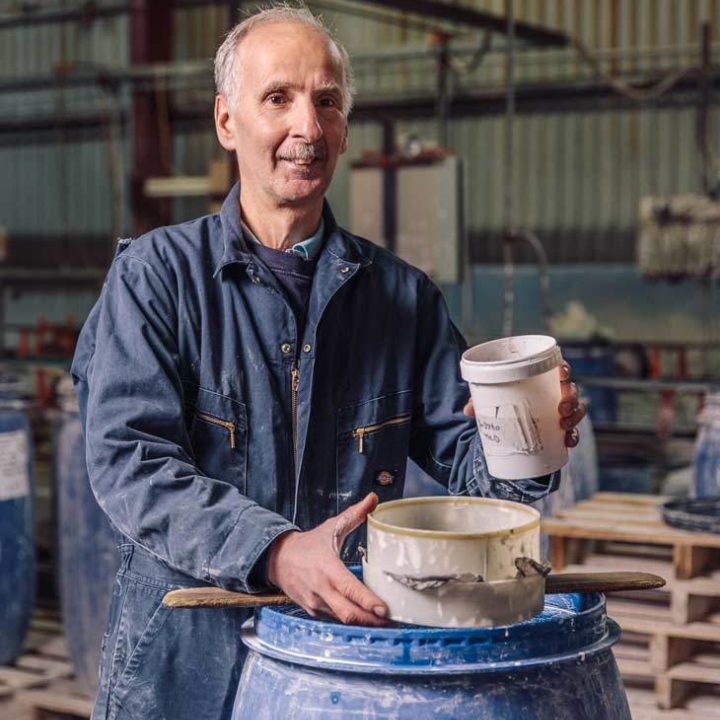 Steve mixing our signature tile glazes into a barrel with our factory behind.