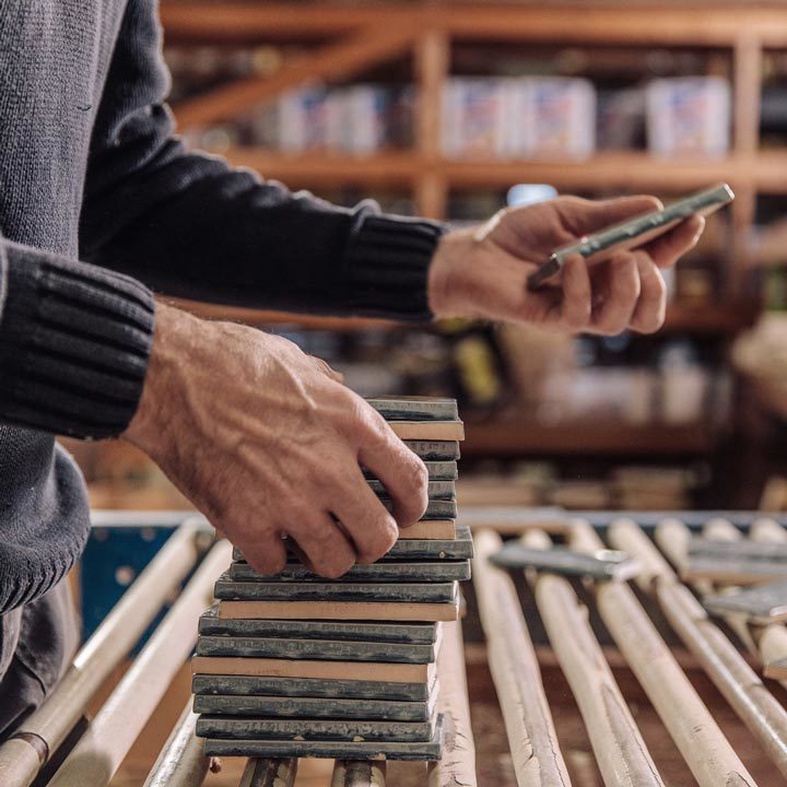 A pile of hand glazed tiles with hands organising them in a tile factory.