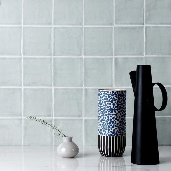 Wall of light blue square wall tiles with a black jug and two vases