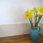 aged crackle wall tiles behind a blue jug of yellow daffodils on a wooden worktop