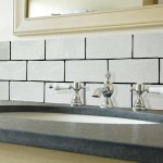 Wall of aged crackle glazed small brick tiles with black grout behind a classic white basin with traditional taps and a grey surface