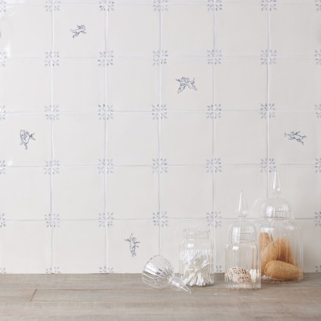 Wall of white square tiles with delft illustration of cherups and ornate corners with white grout behind a selection of glass jars