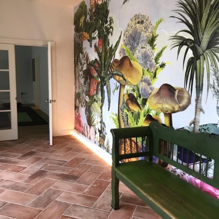 Hallway with terracotta floor tiles laid in a herringbone pattern and vibrant tropical wallpaper and green chair