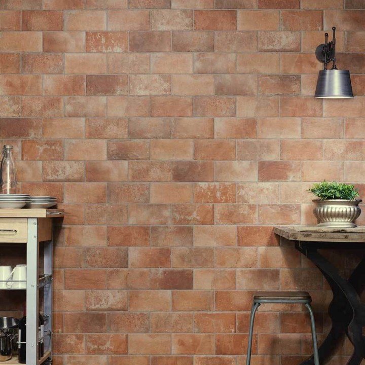 Wall of terracotta brick tiles in a brick bond pattern with grey grout behind a kitchen table an wall light