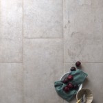 Floor of rectangle pale grey stone effect porcelain floor tiled with beige grout with home accessories on top