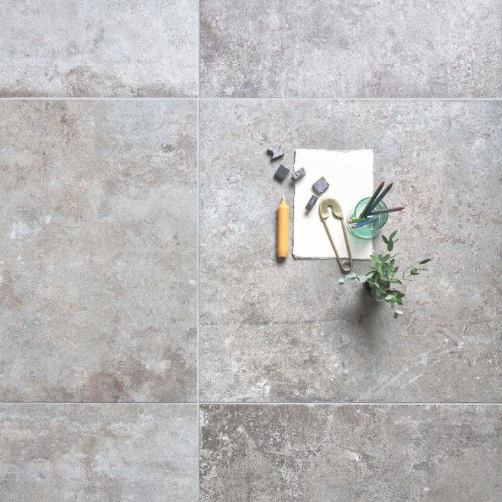 Floor of square warm taupe stone effect porcelain floor tiled with grey grout with home accessories on top