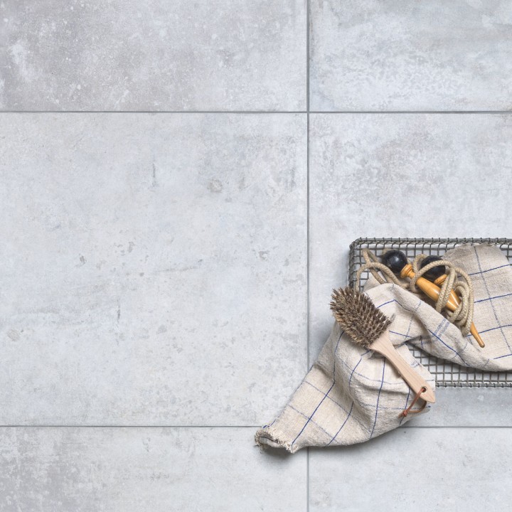 Floor of square pale grey stone effect porcelain floor tiled with grey grout with an oven tray on top