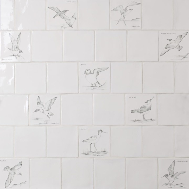 Wall of hand painted coastal bird square tiles in a charcoal style with an antique background paired with plain antique white tiles