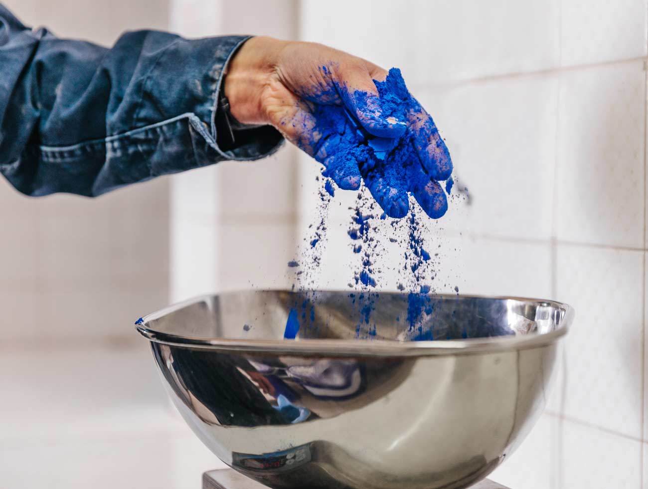 Close up of hand sprinkling blue paint pigment into a metal bowl