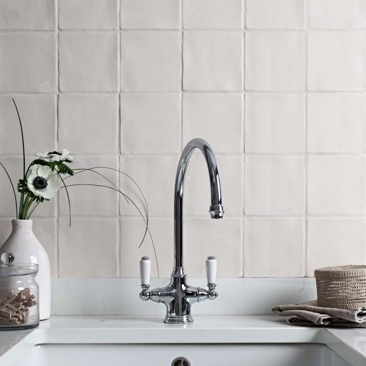 Wall of antique white square tiles behind a belfast sink with traditional silver mixer tap and a vase of flowers