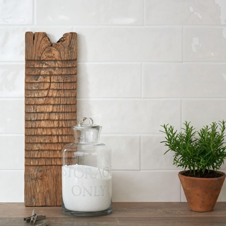 Wall of long white brick tiles with white grout behind a dark wood work top, chopping board, glass jar and house plant