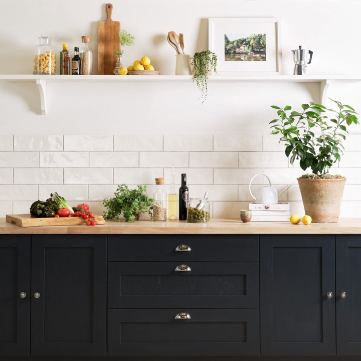 Wall of white long brick tiles with medium grey grout paired with an oak worktop and navy kitchen cabinets