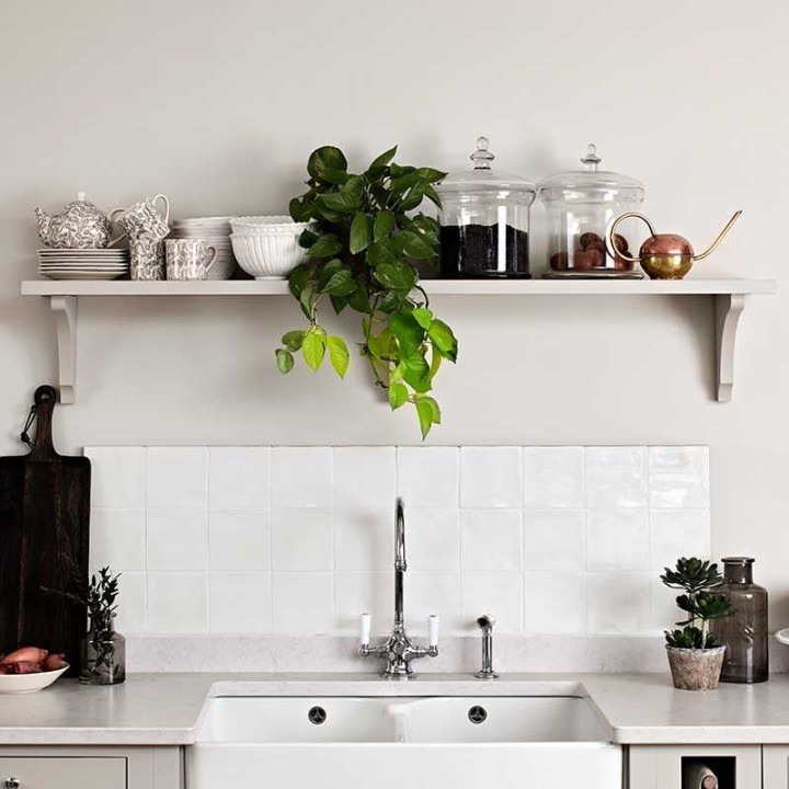 Sink splashback of off white gloss square tiles behind a belfast sink and warm grey kitchen cabinets
