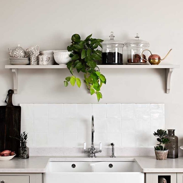 Sink splashback of off white gloss square tiles behind a belfast sink and warm grey kitchen cabinets
