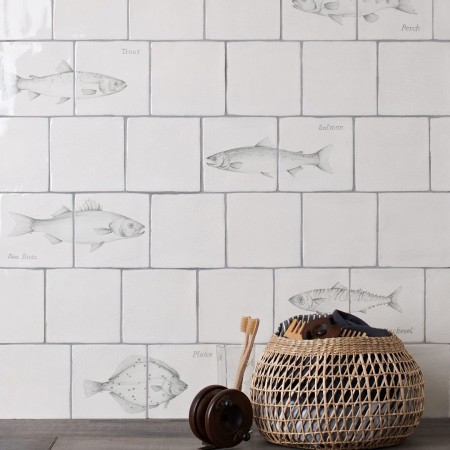 Wall of antique white tiles and pairs of fish tiles hand painted with fish motifs with medium grey grout
