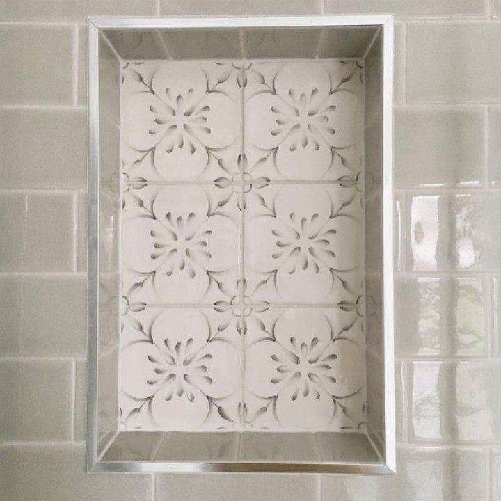 handpainted patterned tiles on the back wall of a small shower niche surrounded by grey tiles and chrome trim