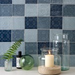 Wall of four shades of rustic blue square tiles with hand piped patterns with medium grey grout behind home accessories
