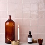 Wall of blush pink handmade square tiles with white grout behind home accessories