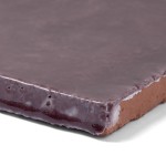 Corner of artisan rustic burgundy square tile to reveal the handmade terracotta base biscuit