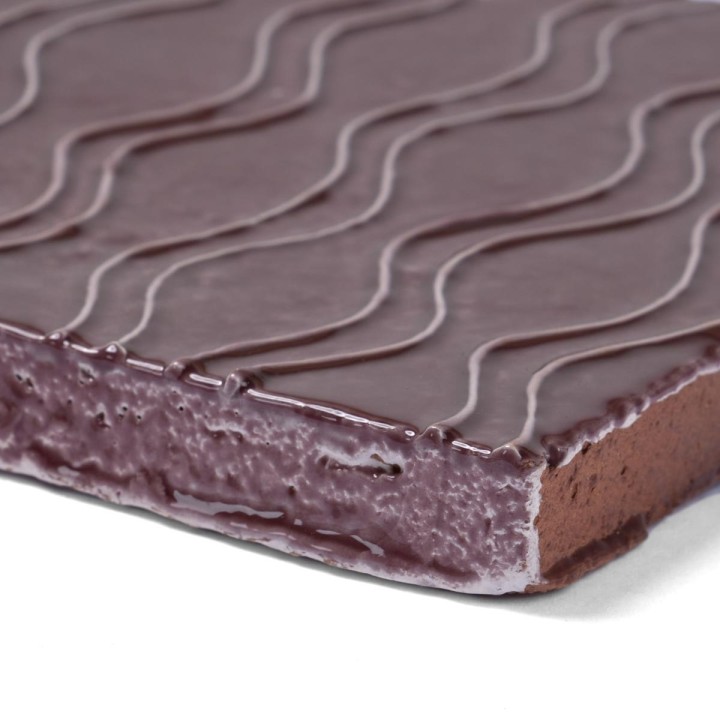 Corner of artisan rustic burgundy square tile with wavy hand piped pattern to reveal the handmade terracotta base biscuit