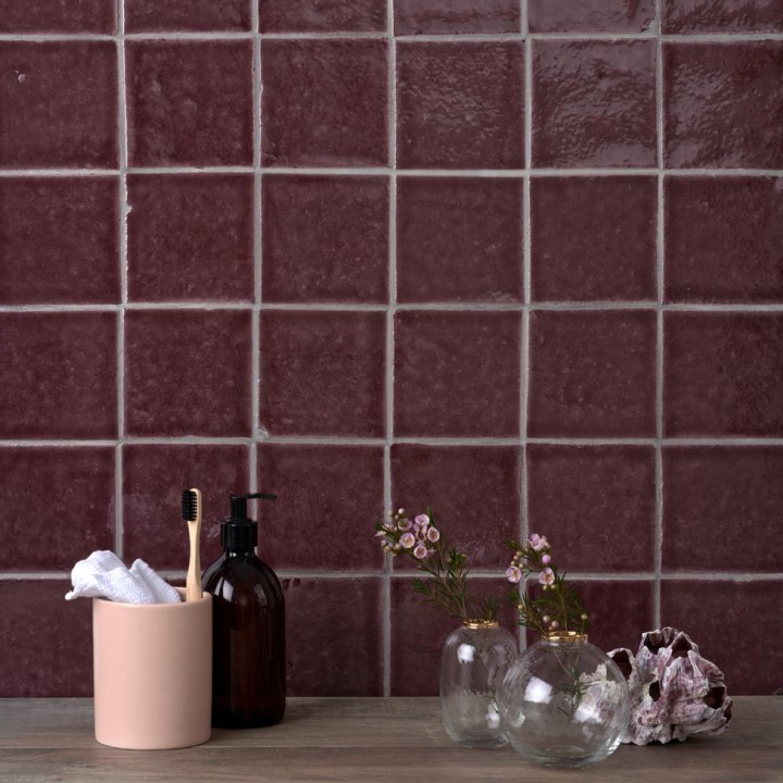 Wall of handmade burgundy red square tiles with grey grout behind bathroom accessories